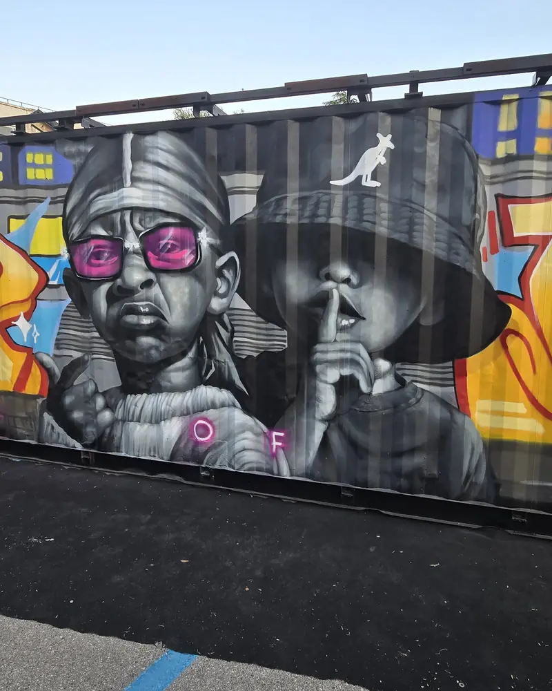 Murale di due character con cappelli e occhiali rosa, dipinto a spray