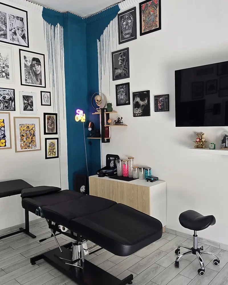Interno dello studio: lettino da tatuaggio, parete blu e cornici alle pareti